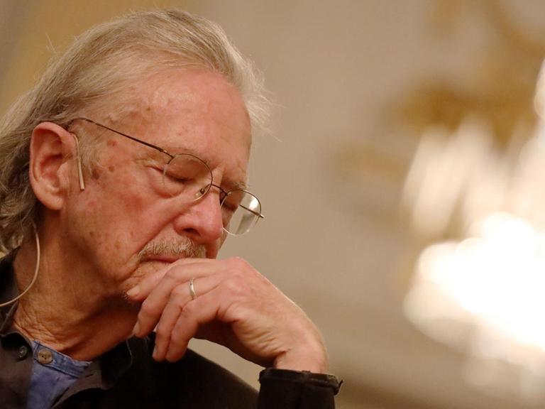 Schriftsteller Peter Handke auf der Pressekonferenz zum Literaturnobelpreis am 5. Dezember in Stockholm. Ein älterer Herr sitzt auf einem Stuhl, hat den Kopf gesenkt und hat die Augen geschlossen.