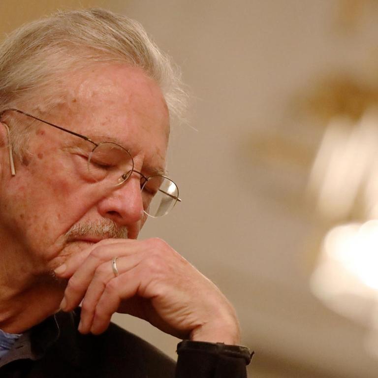 Schriftsteller Peter Handke auf der Pressekonferenz zum Literaturnobelpreis am 5. Dezember in Stockholm. Ein älterer Herr sitzt auf einem Stuhl, hat den Kopf gesenkt und hat die Augen geschlossen.