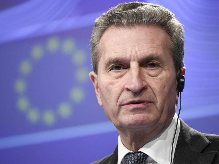 Oettinger steht vor einer blauen Wand mit den EU-Sternen.