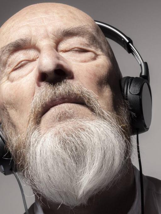 Ein alter Mann mit grauem Vollbart hört entspannt Musik mit Kopfhörern