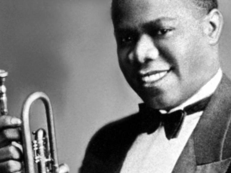 Louis Armstrong im Alter von 19 Jahren, der in Bühnenkleidung lachend sein Instrument präsentiert.