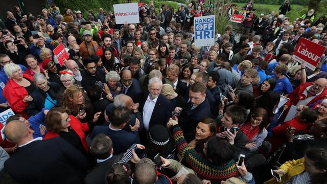 Corbyn steht inmitten einer großen Menschenmenge, um ihn herum Security-Leute. Einige Anhänger tragen "Vote Labour"-Schilder.