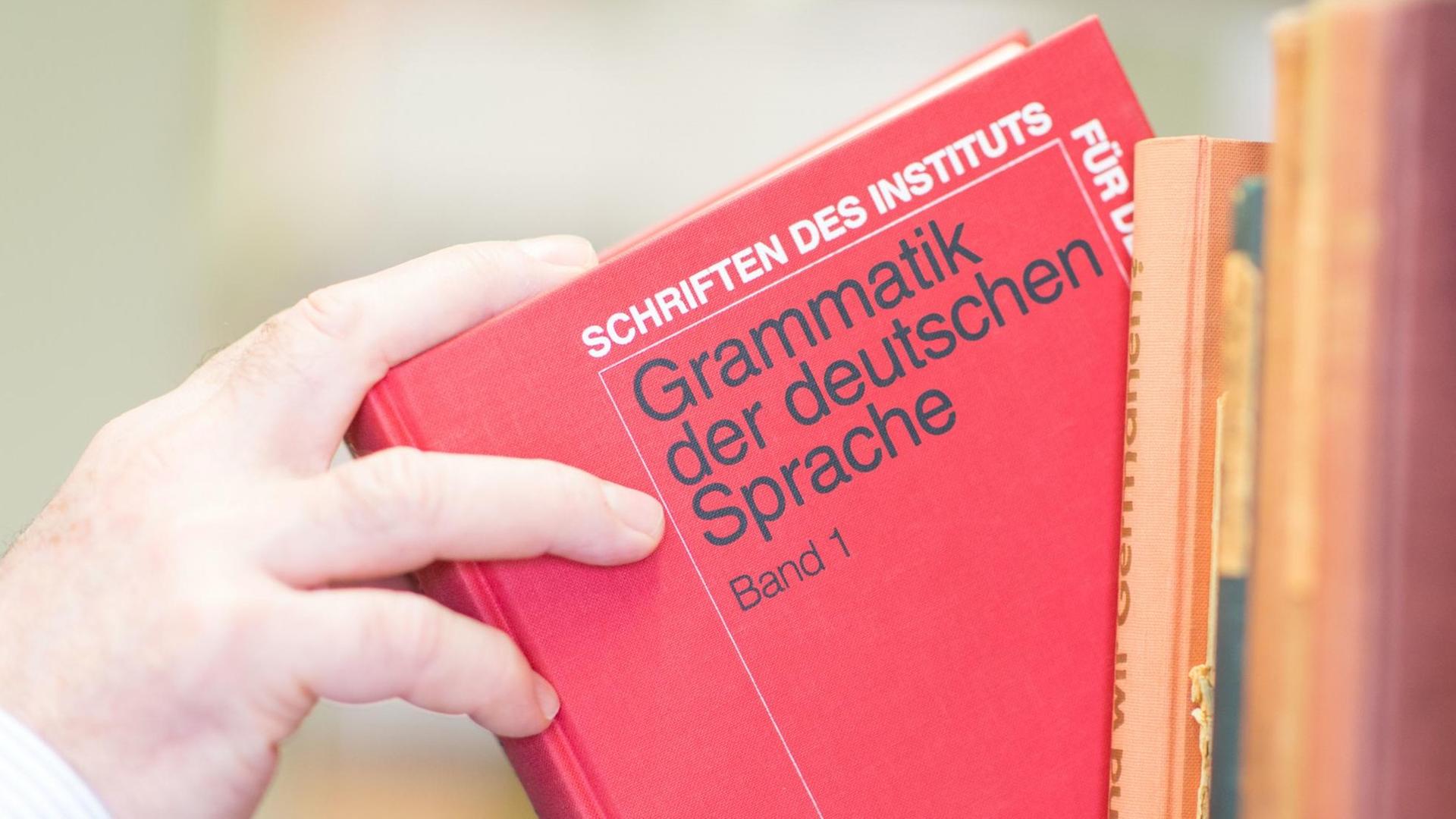 Ein Buch mit der Aufschrift "Grammatik der deutschen Sprache" wird aus einem Bücherregal genommen Ein Buch mit der Aufschrift "Grammatik der deutschen Sprache" wird aus einem Bücherregal genommen