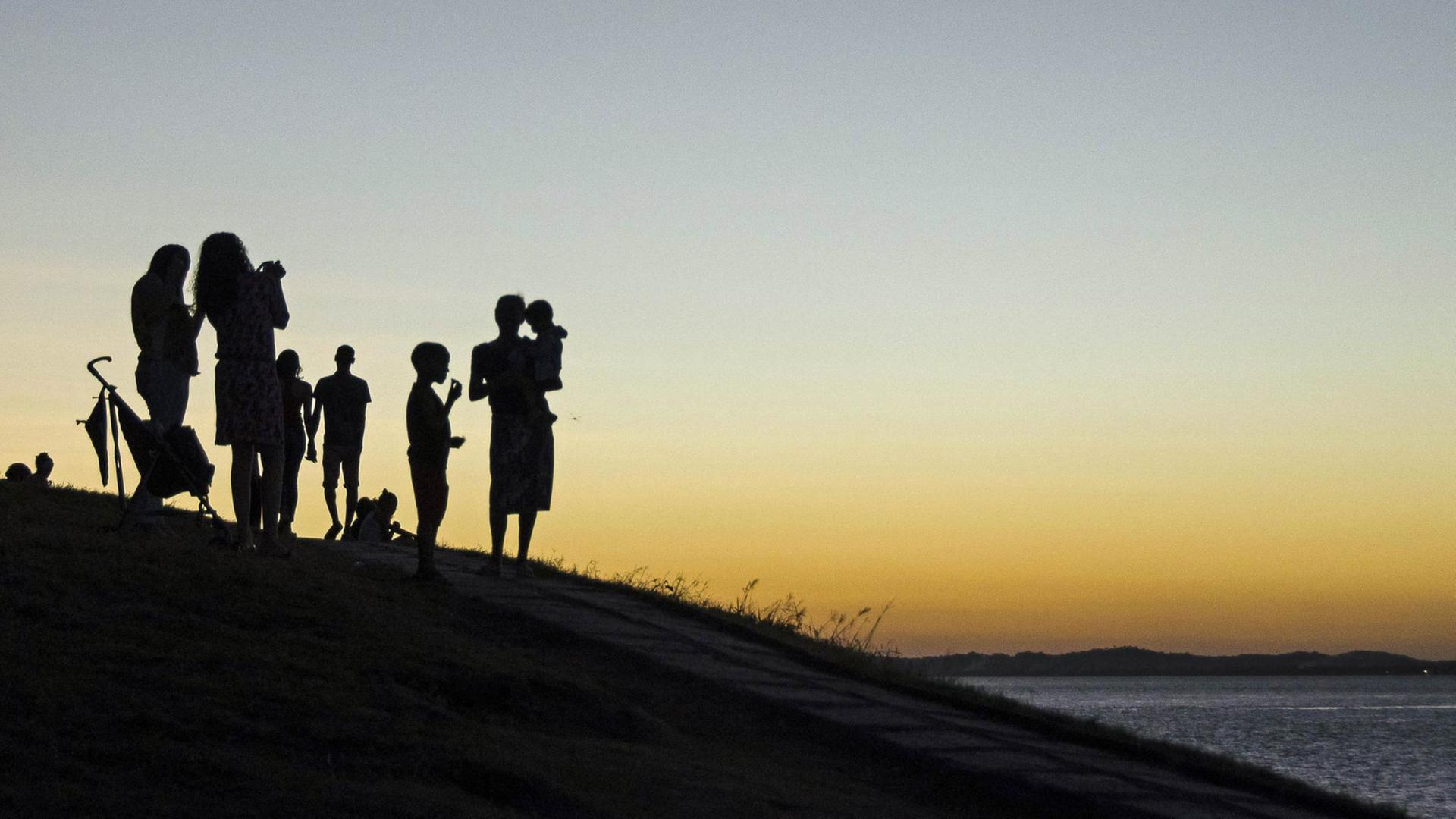 Personen mit Kindern im Gegenlicht beim Sonnenuntergang am Wasser Personen mit Kindern im Gegenlicht beim Sonnenuntergang am Wasser