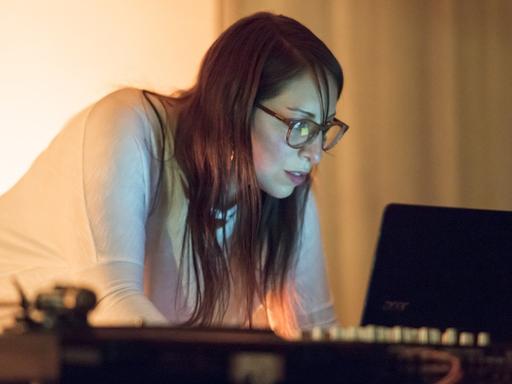 Die Klangkünstlerin Sol Rezza arbeitet an einem Laptop und schaut auf den Bildschirm. Im Vordergrund steht ein Plattenspieler.