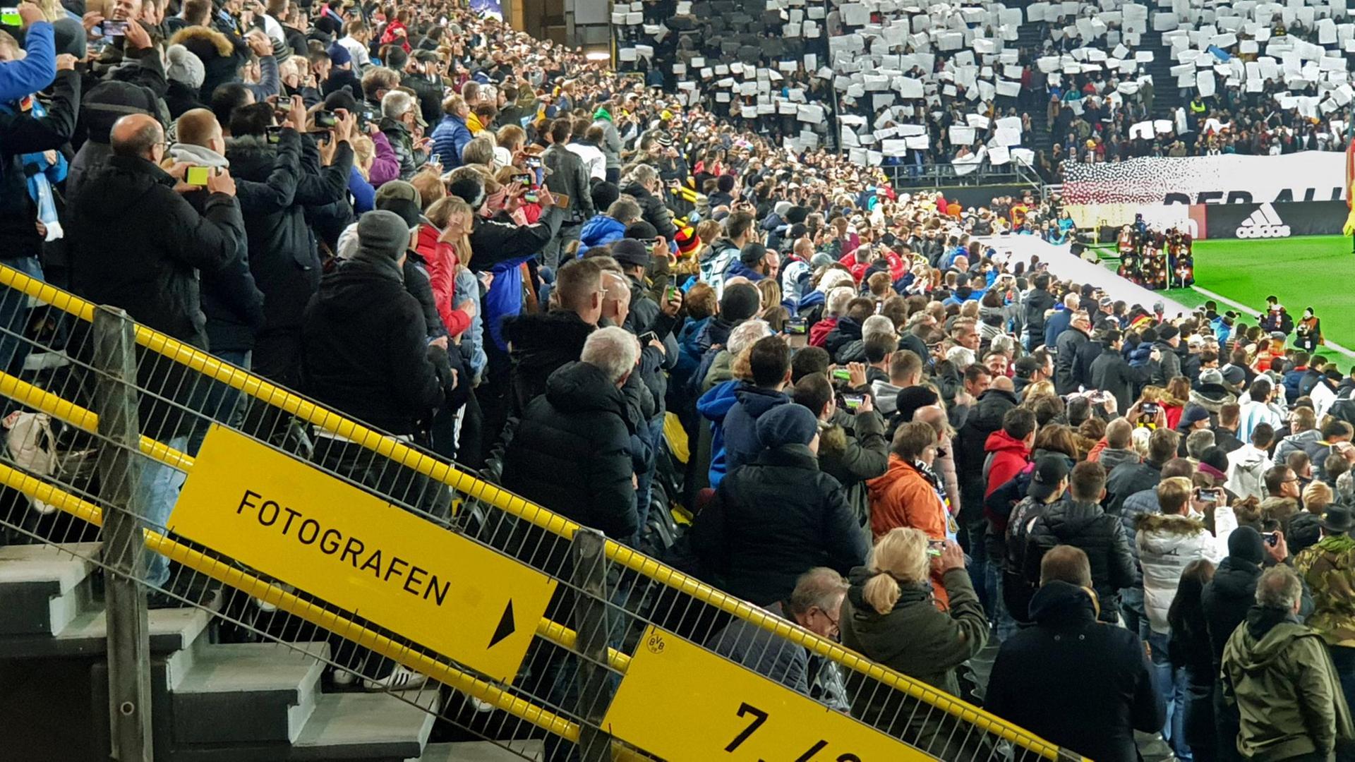 Viele Zuschauer stehen in einem Stadion und gucken Fußball.