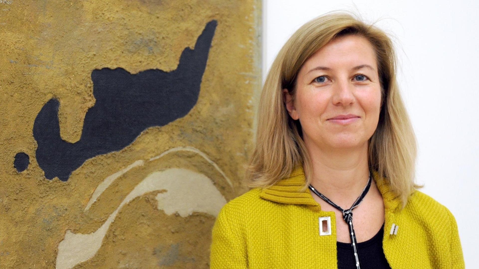 Ulrike Groos, Direktorin des Kunstmuseums in Stuttgart, steht mit Strickjacke vor einem abstraktem Bild.