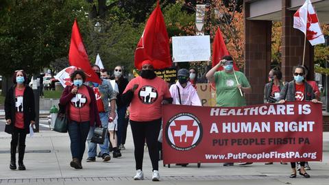Demonstranten mit einem roten Transparent auf dem übersetzt steht: Gesundheitsversorgung ist ein Menschenrecht.