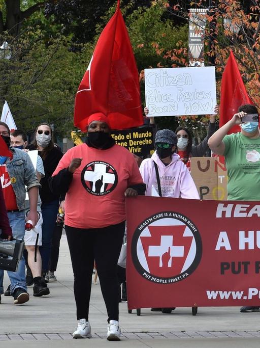 Demonstranten mit einem roten Transparent auf dem übersetzt steht: Gesundheitsversorgung ist ein Menschenrecht.