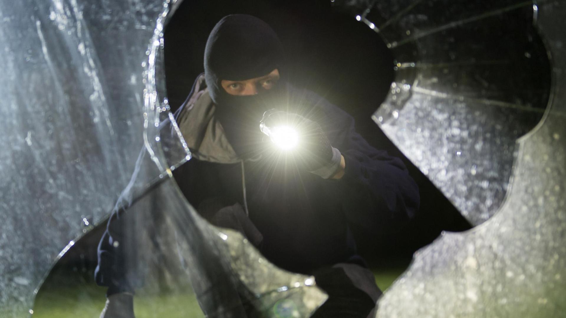 Das Bild zeigt einen fiktiven Einbrecher, er schaut mit Taschenlampe durch eine geborstene Scheibe. Das Bild zeigt einen fiktiven Einbrecher, er schaut mit Taschenlampe durch eine geborstene Scheibe.
