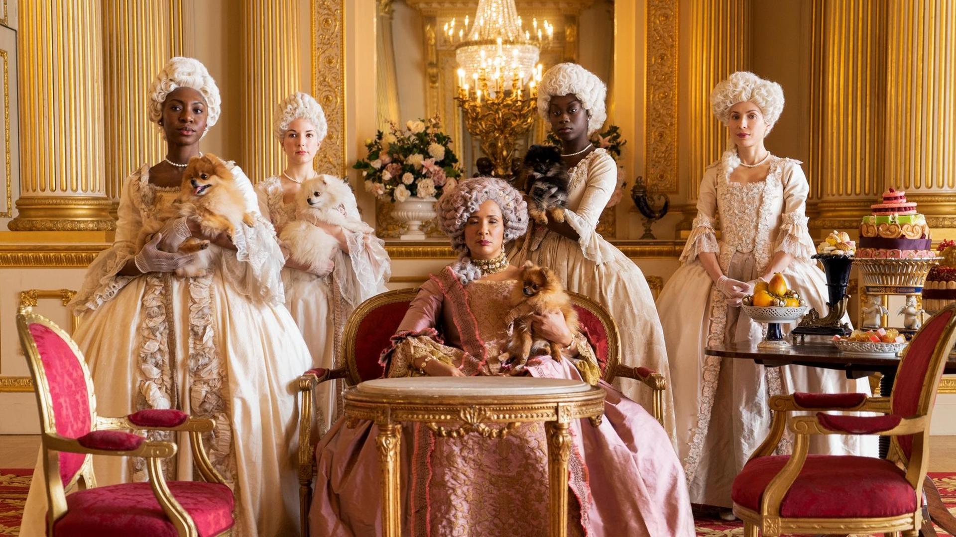 Szene aus der Serie "Bridgerton": Die Queen umringt von adligen Damen / Hofdamen, einige der Frauen sind schwarz, einige weiß.
