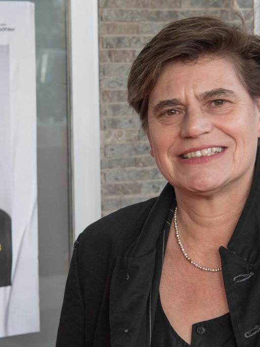 Bettina Böhler neben dem Plakat des Filmes "Schlingensief – In das Schweigen hineinschreien""