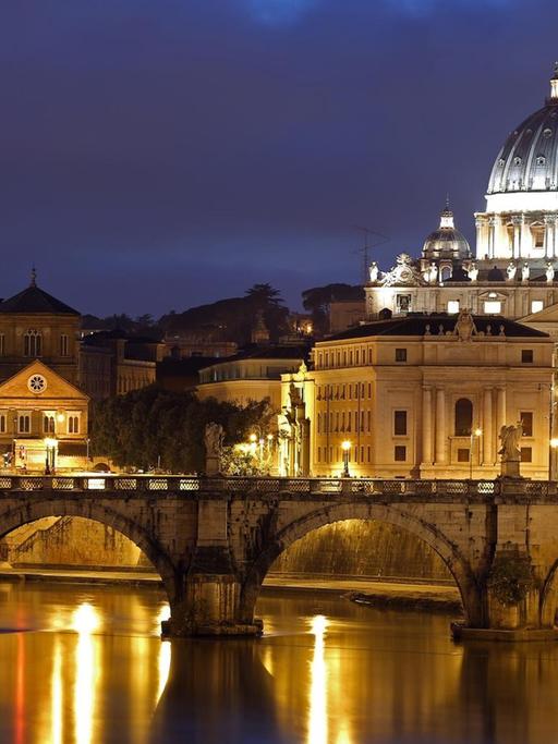 Der Petersdom im Vatikan vor dem abendlichen Himmel. Vorne verläuft die Engelsbrücke über den Tiber.