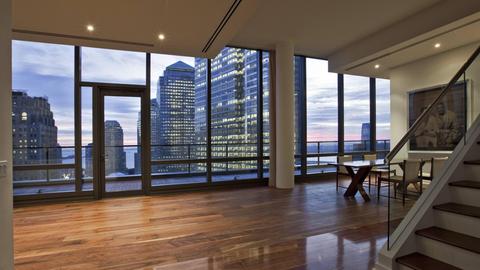 Luxuswohnung in einem Wolkenkratzer in New York. Eine Treppe führt in einen weiträumigen, leeren Wohn- und Küchenbereich, der mit einer Terrasse ausgestattet ist. Die bodentiefen Fenster geben den Blick frei auf die Skyline von Manhattan.