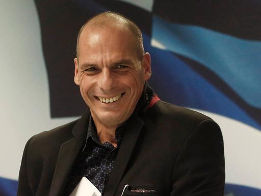 Yanis Varoufakis steckt lachend ein Blatt Papier in die Innentasche seiner Jacke.