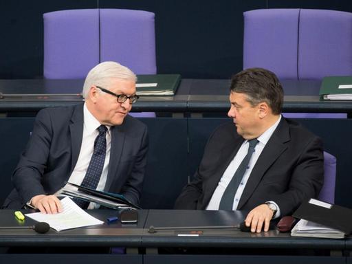 Steinmeier und Gabriel sitzen alleine in schwarzen Anzügen auf der Regierungsbank und reden. Die Sitzreihe hinter ihnen ist leer.