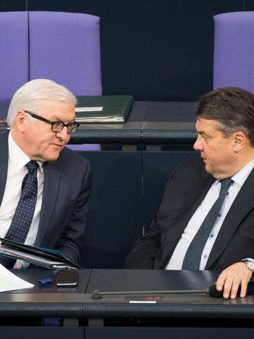 Steinmeier und Gabriel sitzen alleine in schwarzen Anzügen auf der Regierungsbank und reden. Die Sitzreihe hinter ihnen ist leer.
