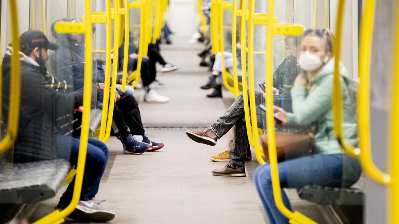 Fahrgäste sitzen in einer U-Bahn, wobei eine Frau einen Mundschutz trägt. 