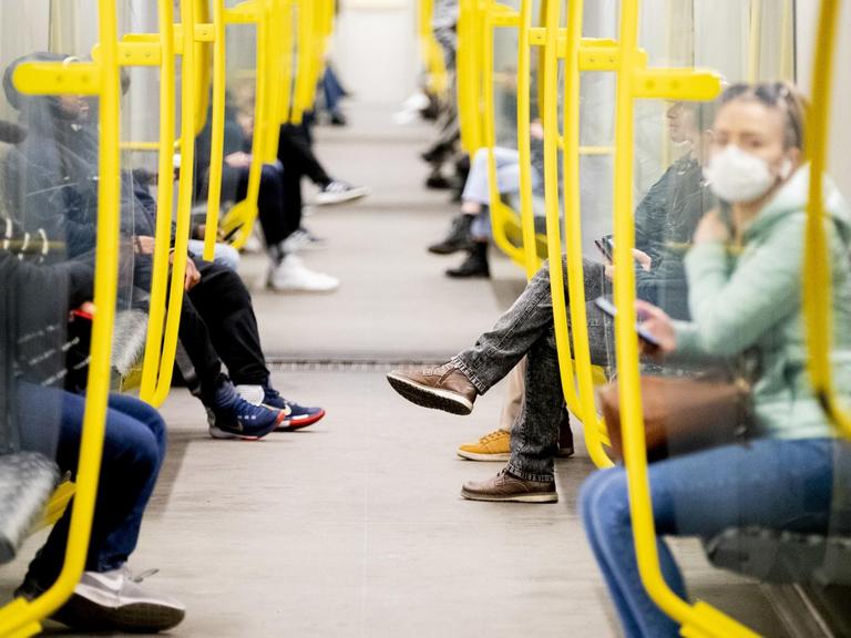 Fahrgäste sitzen in einer U-Bahn, eine Frau trägt einen Mundschutz.