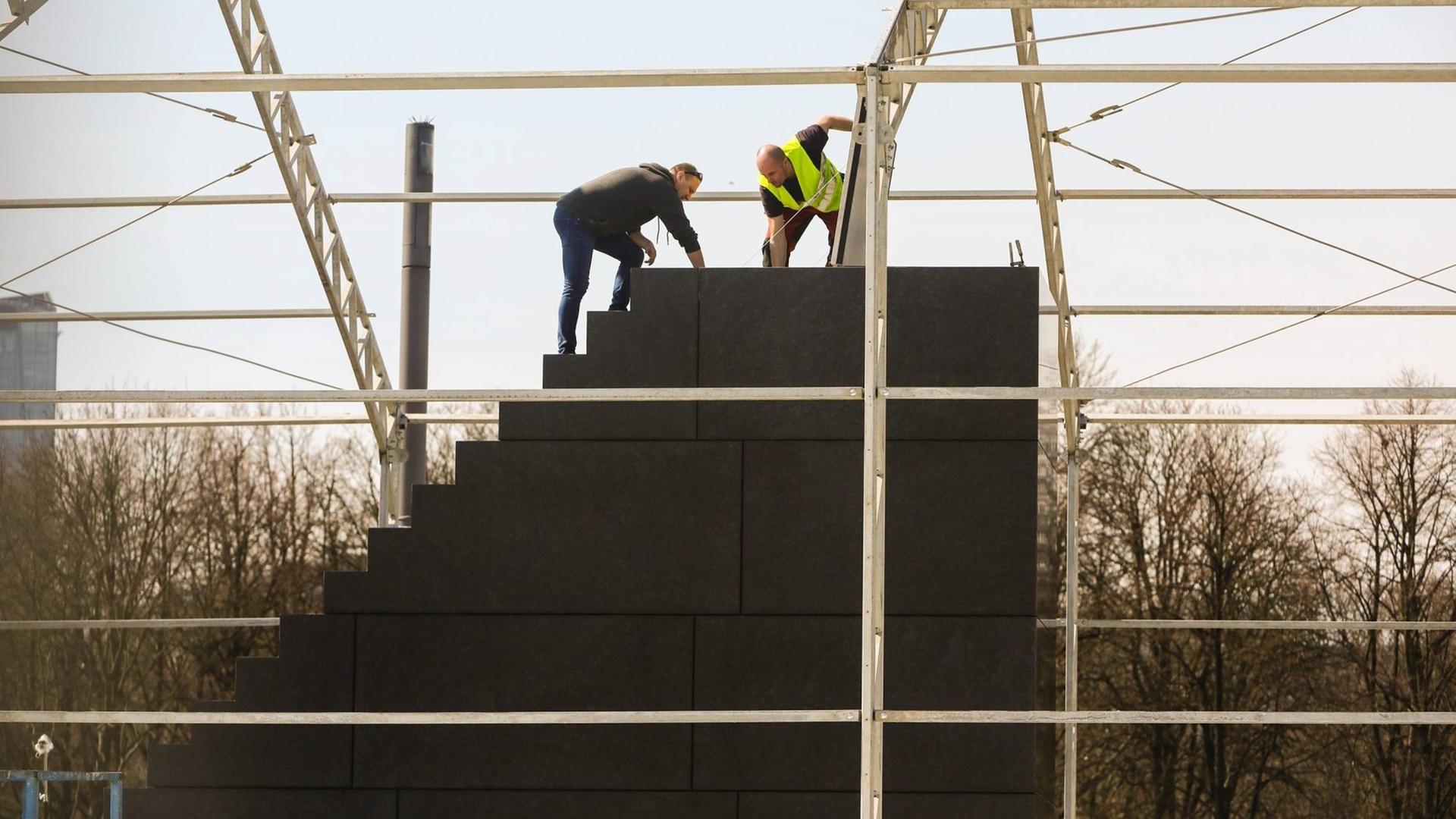 Ein Blick durch das Baugerüst auf das neue Denkmal am Pilsudski-Platz in Warschau zur Erinnerung an die Opfer des Flugzeug-Unglücks bei Smolensk am 10.04.2010. 2 Arbeiter auf dem Steinblock und Wenige Tage vor seiner Einweihung. 2 Arbeiter stehen auf dem noch nicht ganz fertigen Steinblock. Ein Blick durch das Baugerüst auf das neue Denkmal am Pilsudski-Platz in Warschau zur Erinnerung an die Opfer des Flugzeug-Unglücks bei Smolensk am 10.04.2010. 2 Arbeiter auf dem Steinblock und Wenige Tage vor seiner Einweihung. 2 Arbeiter stehen auf dem noch nicht ganz fertigen Steinblock.
