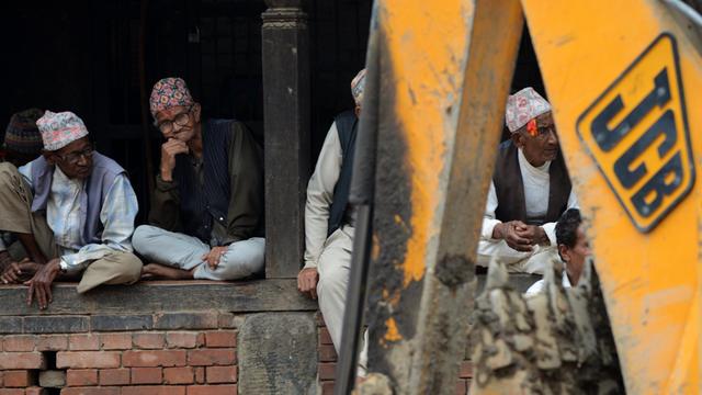 Nepalesen sitzen auf einer Mauer vor der ein Bagger steht.