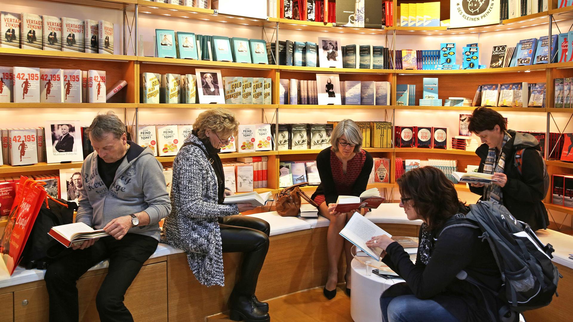 Vier Frauen und ein Mann sitzen vor einer Bücherwand und lesen. Vier Frauen und ein Mann sitzen vor einer Bücherwand und lesen.