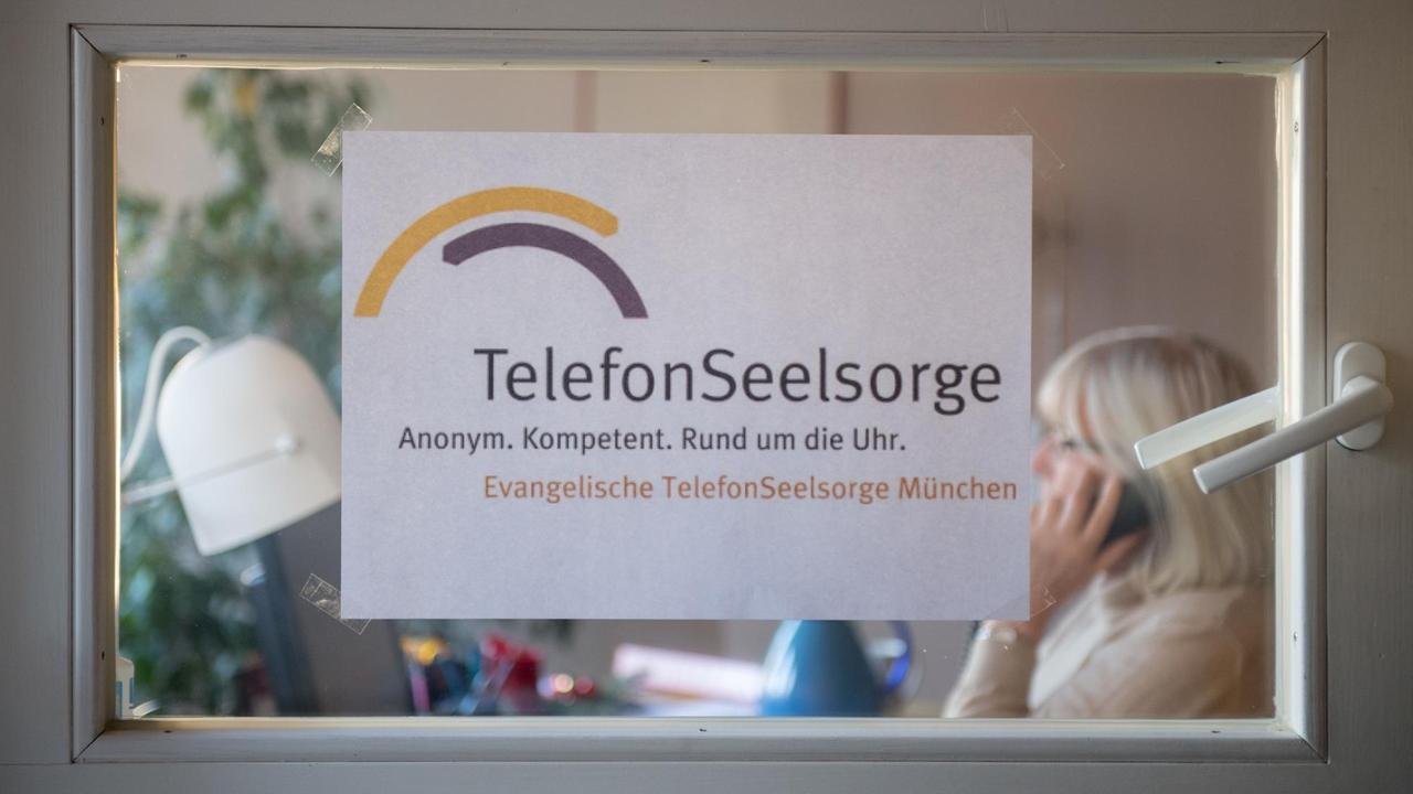 Hinter einer Tür mit der Aufschrift "TelefonSeelsorge" hält eine ehrenamtliche Mitarbeiterin einen Telefonhörer in der Hand. Hinter einer Tür mit der Aufschrift "TelefonSeelsorge" hält eine ehrenamtliche Mitarbeiterin einen Telefonhörer in der Hand.