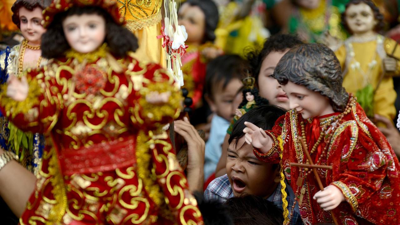 Philippinische Katholiken halten Puppen von Jesus als Kind in die Höhe.