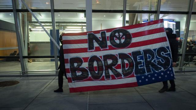 Menschen halten am internationalen Flughafen in New York ein Plakat hoch. Darauf steht: "No Borders".