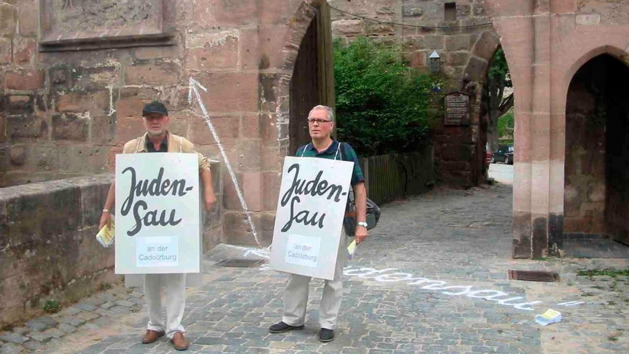 Die Künstler Wolfram Kastner (links) und Günter Wangerin demonstrieren gegen ein umstrittenes Relief an der Cadolzburg im mittelfränkischen Landkreis Fürth. Die Künstler Wolfram Kastner (links) und Günter Wangerin demonstrieren gegen ein umstrittenes Relief an der Cadolzburg im mittelfränkischen Landkreis Fürth.