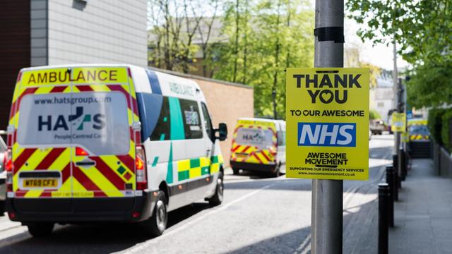 "Thank you NHS" steht auf einem Zettel an einem Laternenpfahl an einer Londoner Straße, auf der Krankenwagen vorbeifahren, 14. April 2020