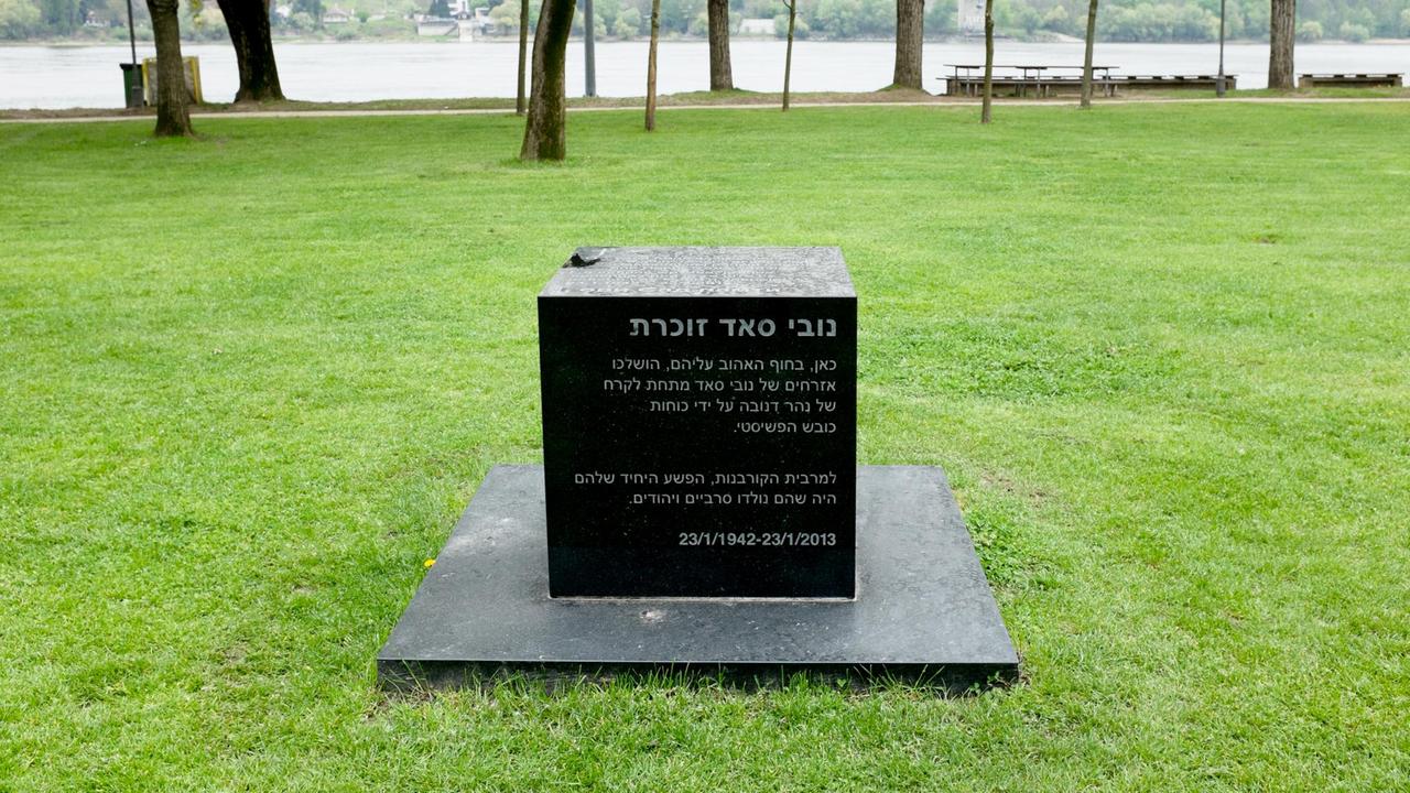 Schwarzer Gedenkstein auf einer Wiese, im Hintergrund ein Fluss.