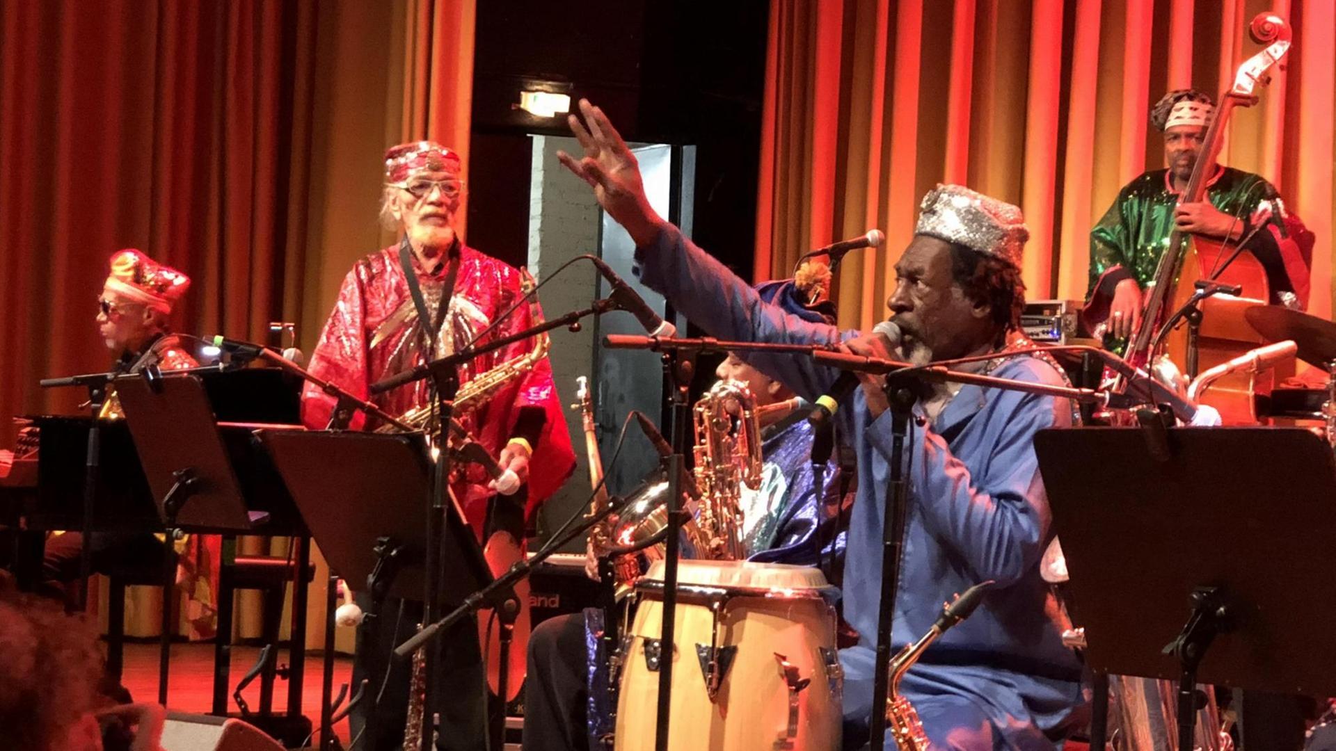 Auf dem Bild ist das Sun Ra Arkestra zu sehen. Die Musiker tragen glitzernde Gewänder. Auf dem Bild ist das Sun Ra Arkestra zu sehen. Die Musiker tragen glitzernde Gewänder.