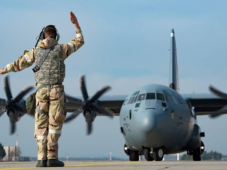 Ein Soldat steht auf dem Rollfeld der US Air Base Ramstein und gibt einem C-1301J Super Hercules Transportflugzeug Kommandos.