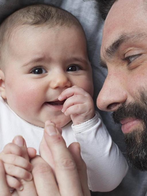 Ein Vater und sein Baby halten sich an den Händen.
