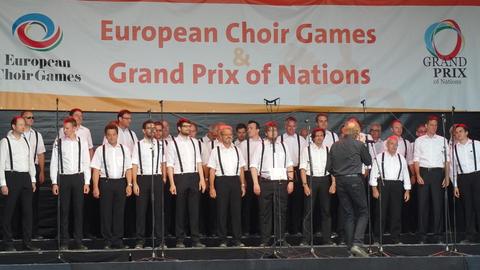 Die Männer des Chores stehen bei den Choir Games in schwarzen Hosen und weißen Hemden auf der Bühne.