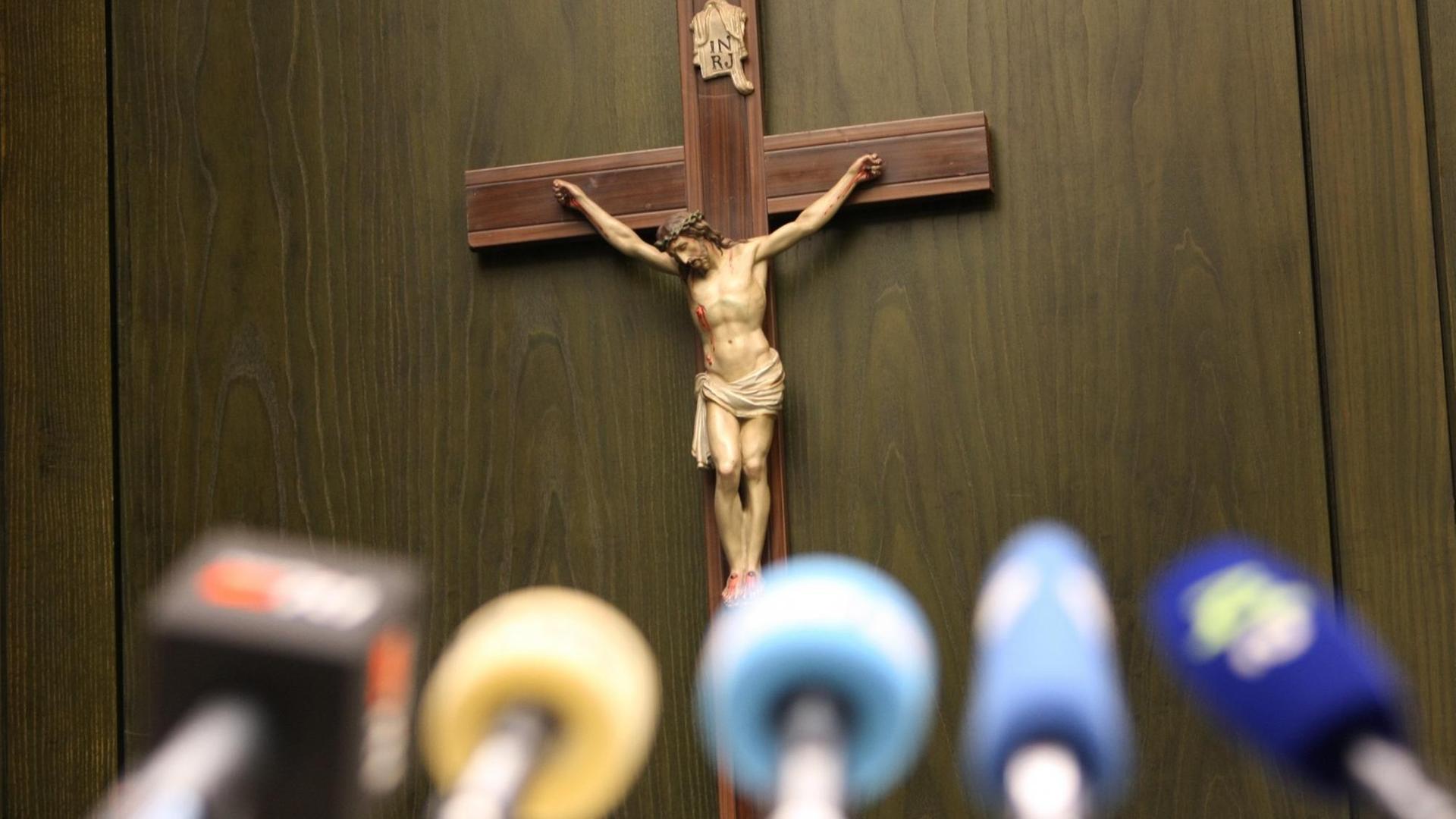 Ein Kreuz hängt bei einer Pressekonferenz vor Mikrofonen an einer Wand. Ein Kreuz hängt bei einer Pressekonferenz vor Mikrofonen an einer Wand.
