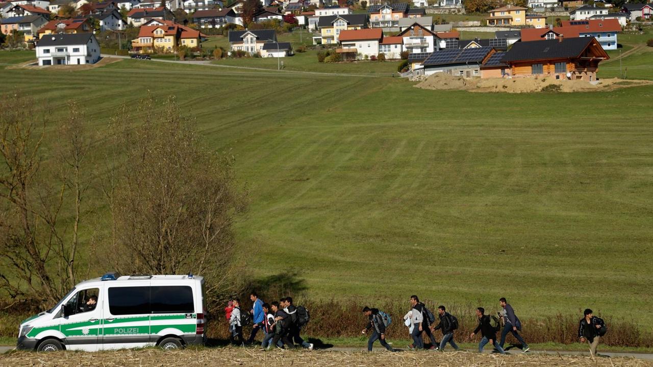 Ein Polizeiwagen und eine Gruppe von Migranten auf einem Feld vor einem bayrischen Dorf. Ein Polizeiwagen und eine Gruppe von Migranten auf einem Feld vor einem bayrischen Dorf.