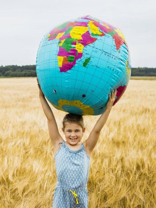 Ein Mädchen steht mit einer großen Weltkugel als Ball in einem Kornfeld.