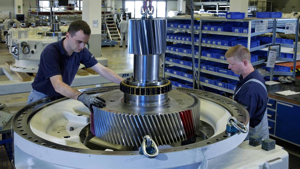 Zwei Arbeiter in Blaumännern hantieren in einer Werkhalle an einer Turbine.