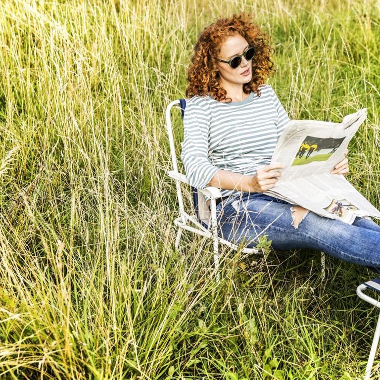 Eine Frau im Grünen liest Zeitung