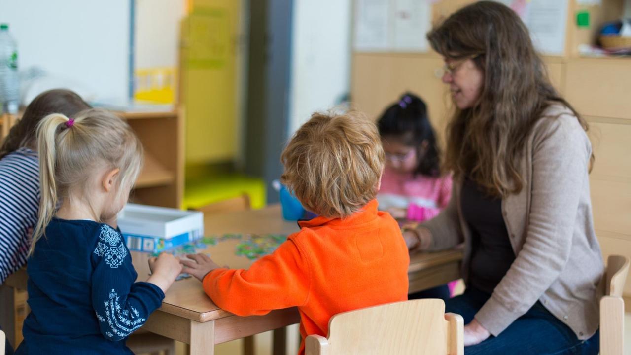 Kinder sitzen am 18.04.2016 in einer Kindertagesstätte in Düsseldorf (Nordrhein-Westfalen) mit einer Erzieherin an einem Tisch.