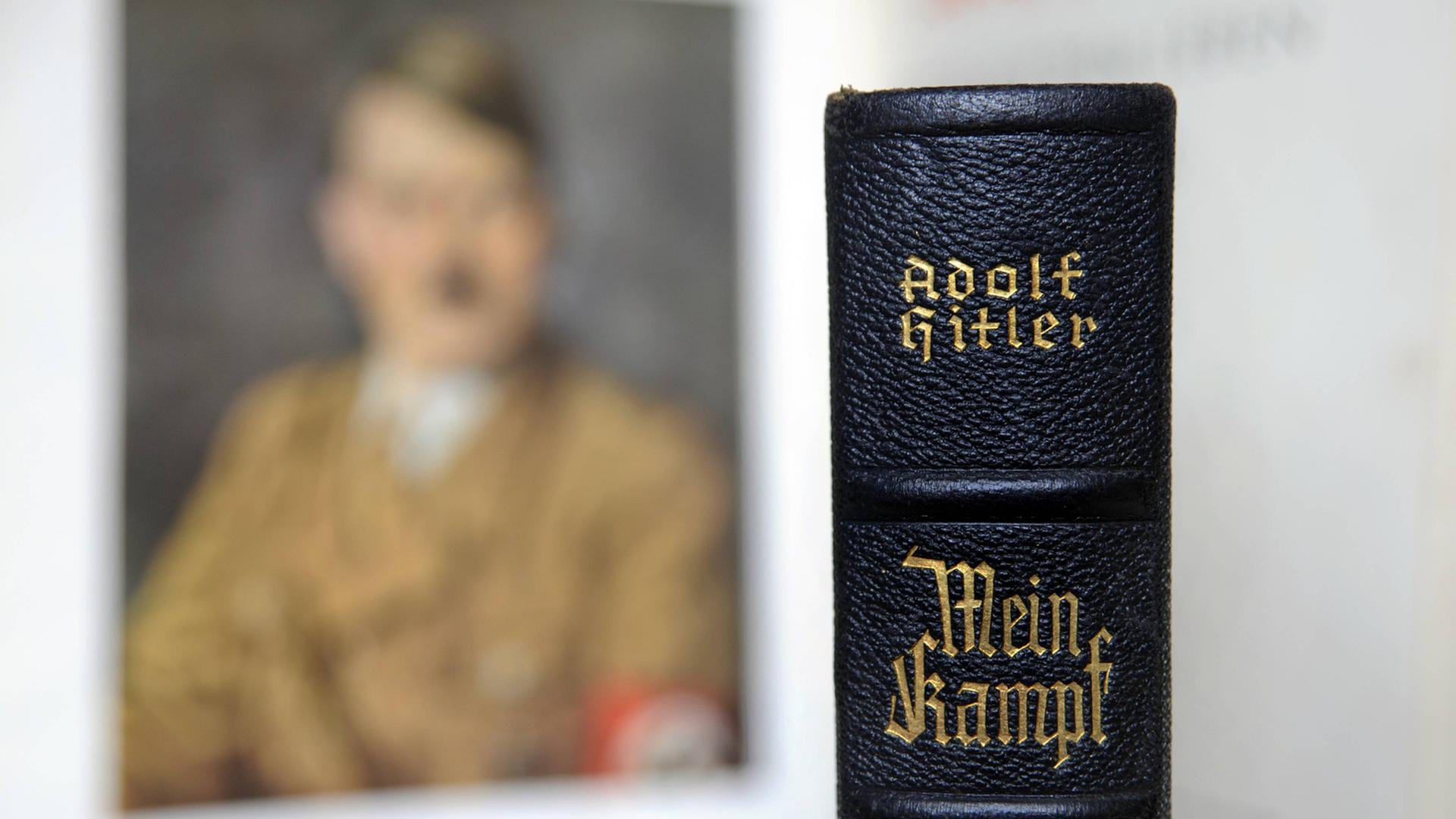 Der Buchrücken einer Ausgabe von Hitlers "Mein Kampf" vor einem unscharfen Porträtbild Hitlers.