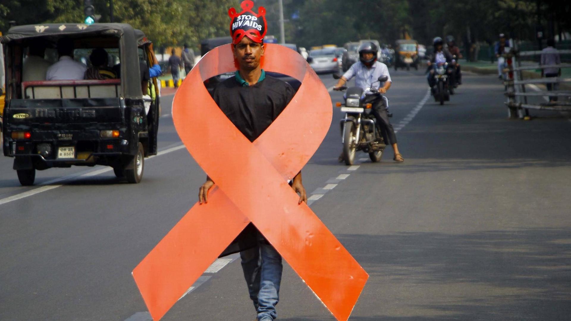 Ein Aktivist trägt ein Aids-Logo um den Körper, das etwa genauso groß ist wie er. Er geht auf einer Straße in Bhubaneswar in Indien. Ein Aktivist trägt ein Aids-Logo um den Körper, das etwa genauso groß ist wie er. Er geht auf einer Straße in Bhubaneswar in Indien.