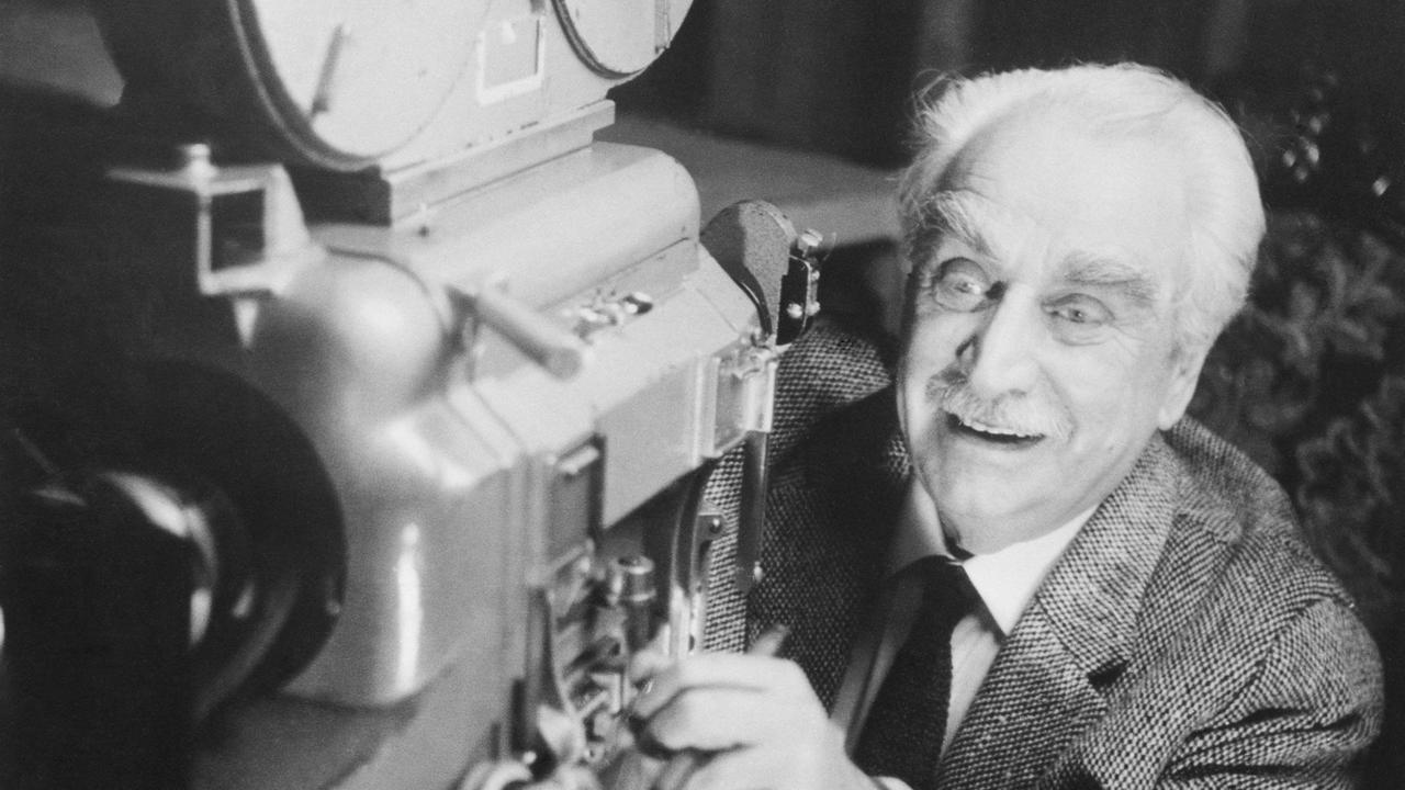 Ein älterer Mann mit weißem Haar steht hinter einer großen Kamera und schaut begeistert auf die Filmspule. Ein älterer Mann mit weißem Haar steht hinter einer großen Kamera und schaut begeistert auf die Filmspule.