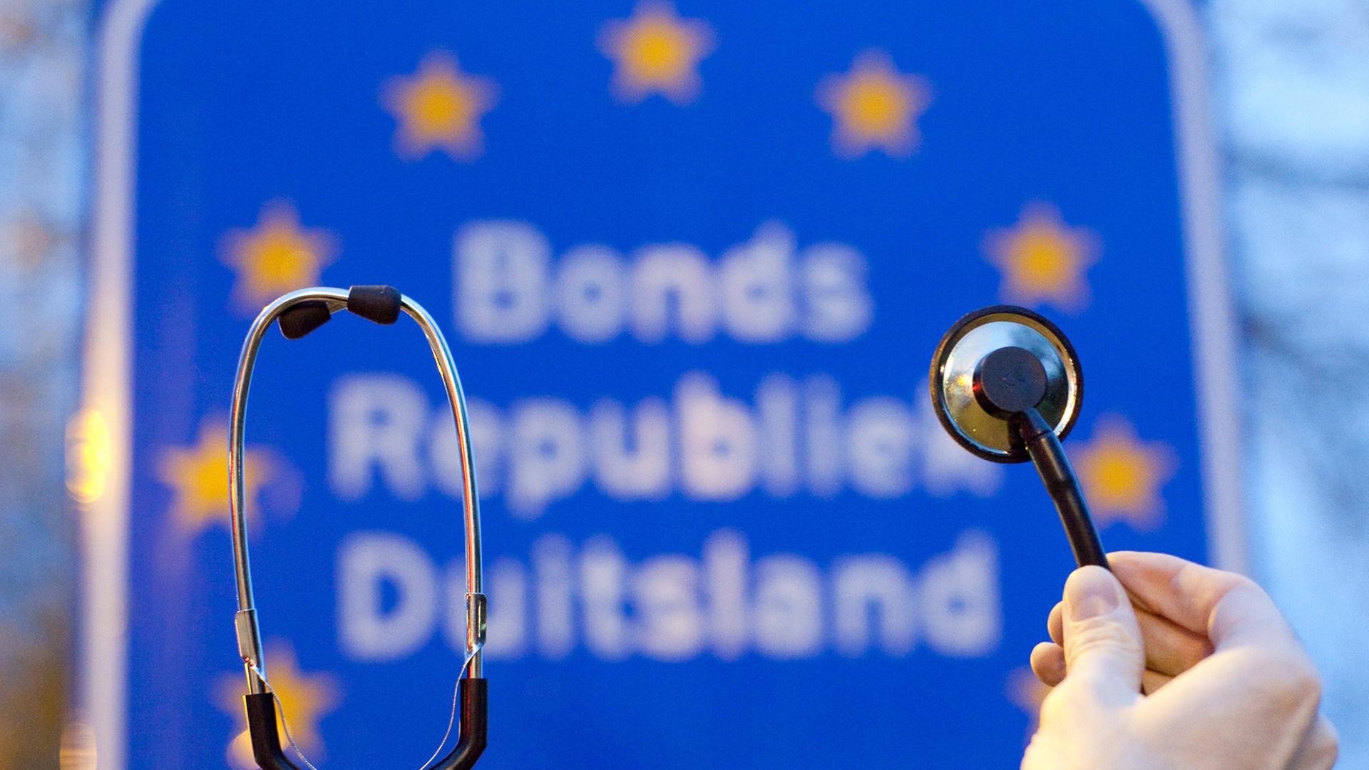 Ein Stethoskop wird vor ein Schild mit der Aufschrift "Bonds Republiek Duitsland" gehalten. Ein Stethoskop wird vor ein Schild mit der Aufschrift "Bonds Republiek Duitsland" gehalten.