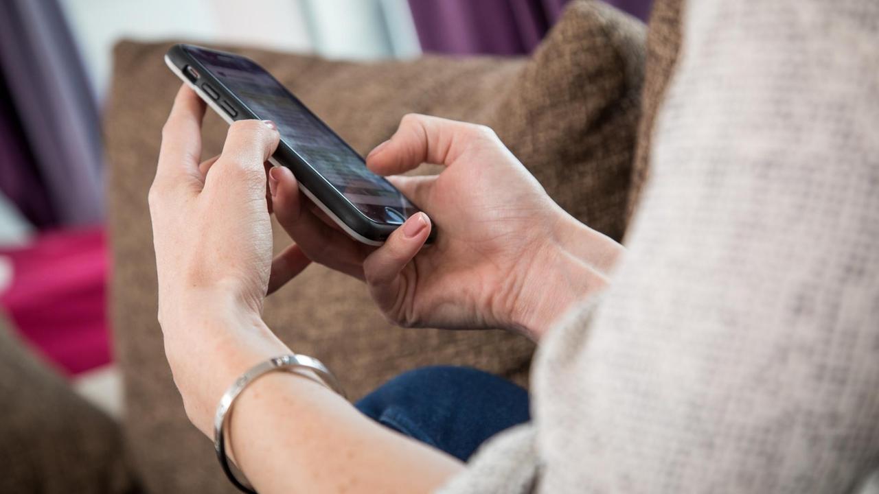 Eine junge Frau nutzt in einer Wohnung in Hamburg einen Instant-Messaging-Dienst auf ihrem Smartphone.  