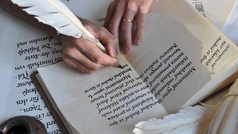 Eine Frau schreibt mit einer Schreibfeder in altertümlicher Schrift.