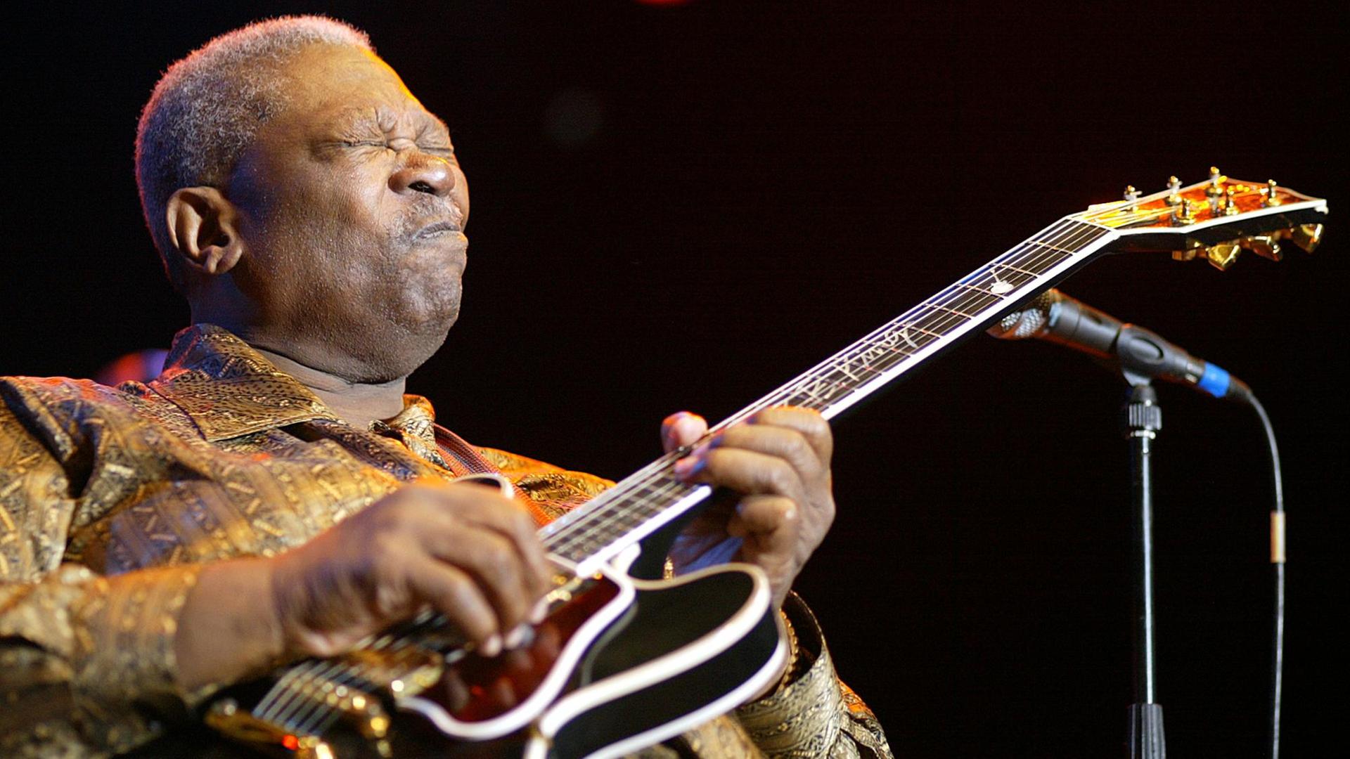 Ein Afroamerikaner mit kurzen grauen Haaren spielt im Sitzen mit geschlossenen Augen Gitarre. Ein Afroamerikaner mit kurzen grauen Haaren spielt im Sitzen mit geschlossenen Augen Gitarre.