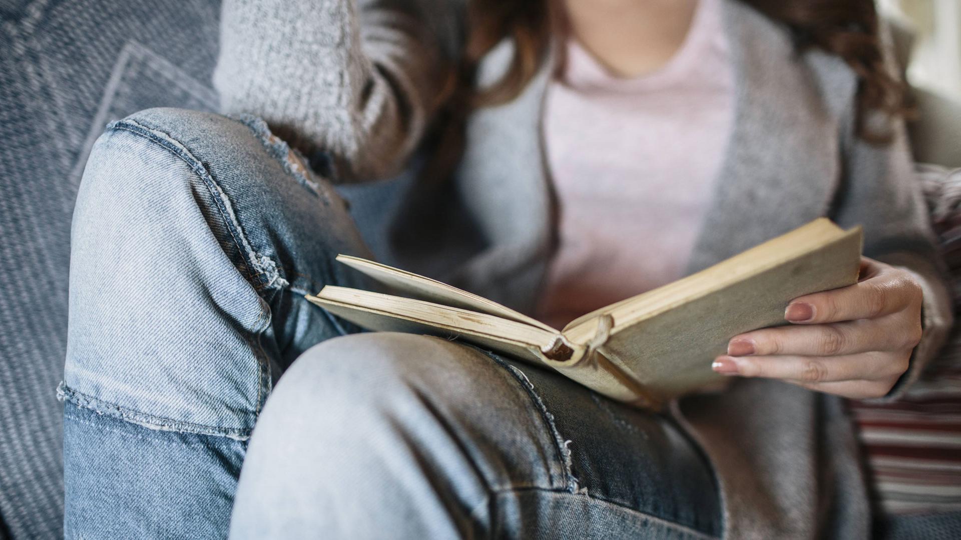 Eine Frau sitzt lesend auf einem Sofa. Das Buch ist der Mittelpunkt des Bildes. Eine Frau sitzt lesend auf einem Sofa. Das Buch ist der Mittelpunkt des Bildes.